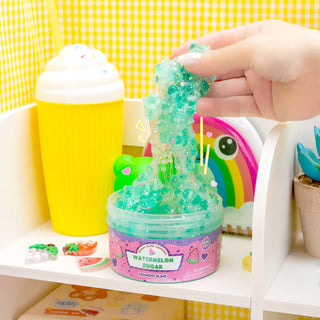 Hand stretching a stretchy, watermelon-scented slime above a container on a shelf.