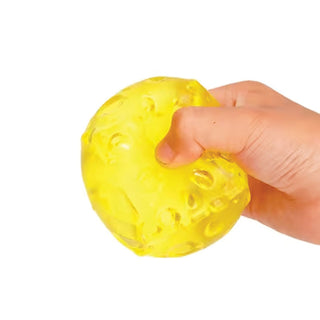 A hand squeezing a translucent yellow stress toy with a bubbly texture against a plain white background.