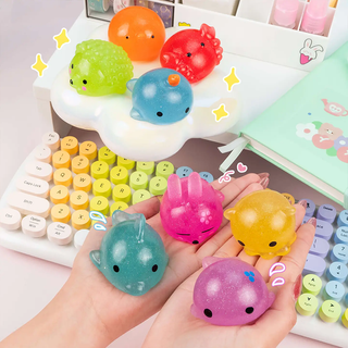 Four colorful squishy toys held in two hands and the other four on a small shelf, with a keyboard and stationery items in the background.