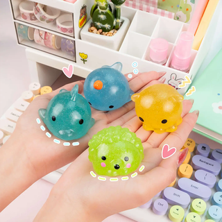 Four colorful squishy toys held in two hands with a decorated desk background.