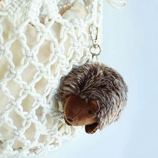 Plush brown hedgehog keychain with a silver clip clipped on a woven bag