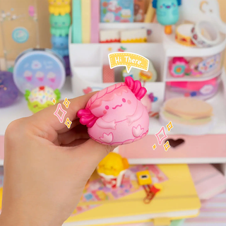 A hand squishing a pink squishy cake-themed axolotl. 